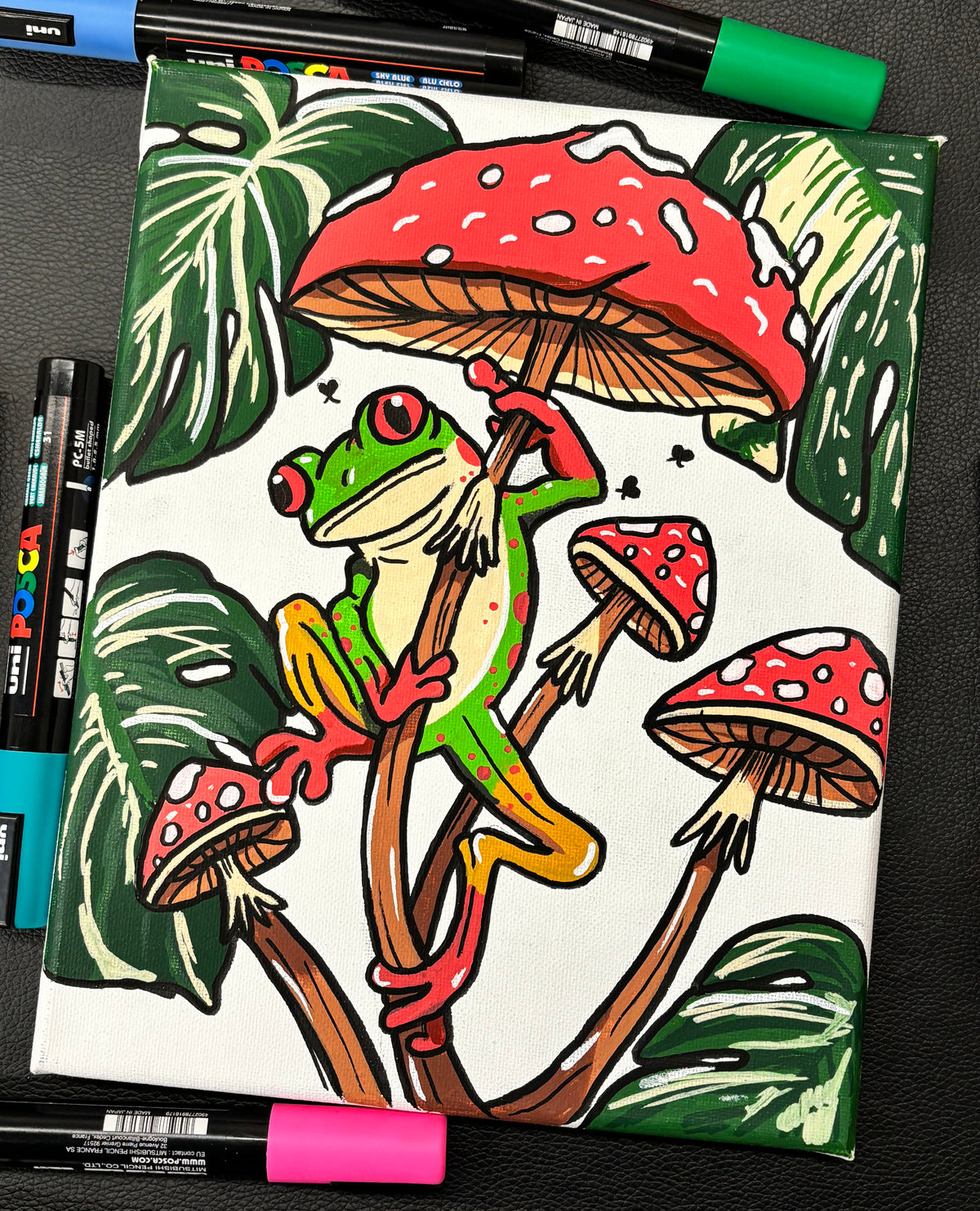 Colorful drawing with a frog and mushroom design, surrounded by markers.