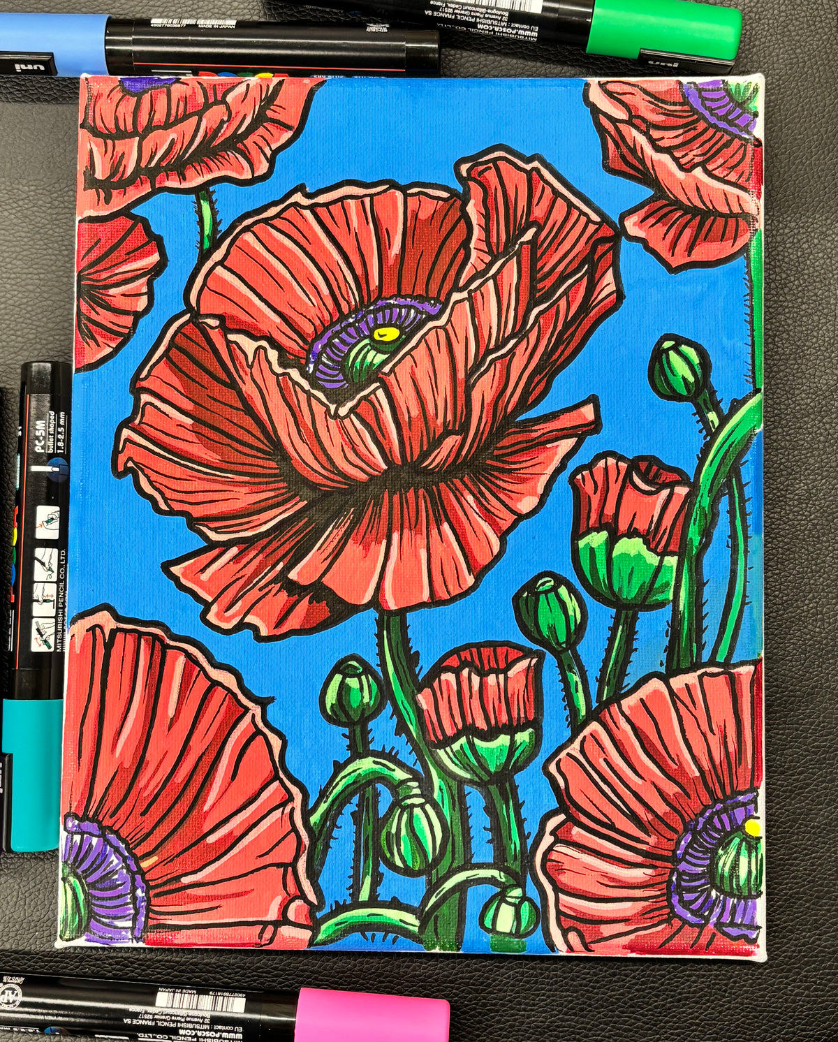 Colorful poppy flower drawing on a blue background with markers around.
